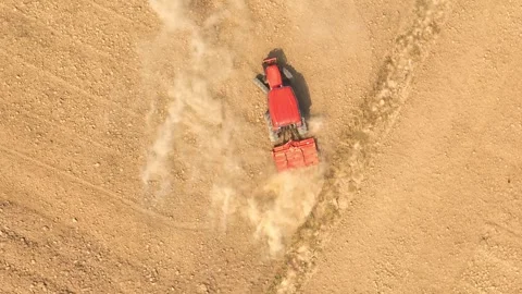 An aerial view shows a red tractor pulling a cultivator across a dry. Stock Footage 274938475