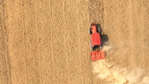 An aerial view shows a red tractor pulling a cultivator across a dry. Stock Footage 274938479