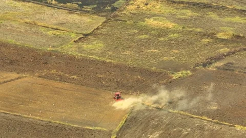 An aerial view shows a red tractor pulling a cultivator across a dry. Stock Footage 274938541