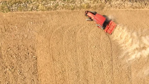 An aerial view shows a red tractor pulling a cultivator across a dry. Stock Footage 274938547