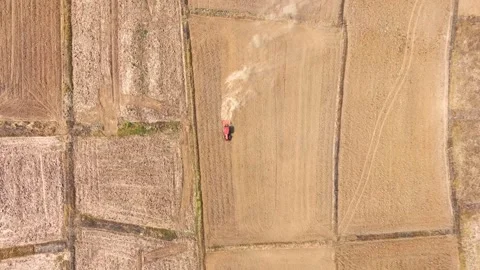 An aerial view shows a red tractor pulling a cultivator across a dry. Stock Footage 274938562