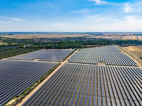 Aerial view shows several rows of solar panels set in fields near a small tow Stock Photos