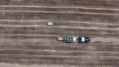 An aerial view shows a tractor pulling a baler, making straw bales in a vast 库存影片 341403903