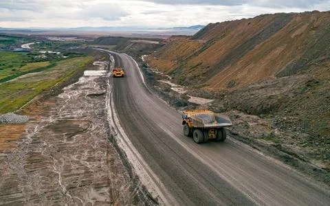 Aerial view shows two large dump trucks transporting materials on a wide dirt Stock Photos
