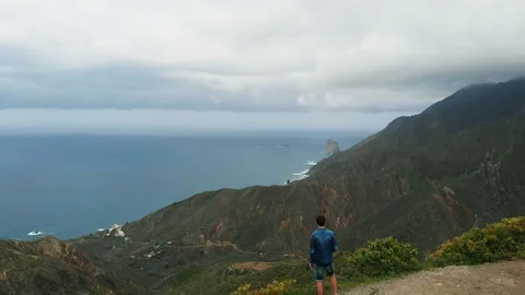 Aerial view. A single man stands on the edge of a mountain, looking at a Stock Footage 111308877