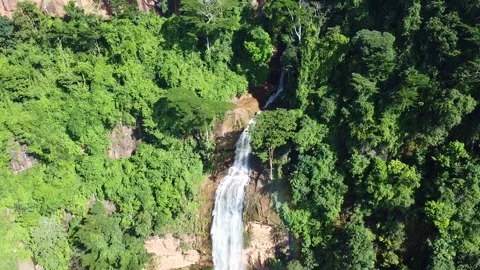 Aerial view of a single waterfall cascading down a rocky cliff surrounded by Stock Footage 316927526