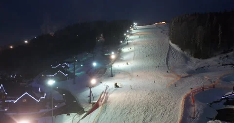 Aerial view of Skiers go Down Ski Slopes near Ski Lifts on Ski Resort at night. Stock Footage 140518183