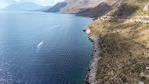 Aerial view of a small boat navigating along rocky coastline with clear waters Stock Footage 345148148