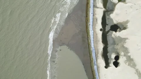 Aerial view of small sea waves crashing onto a geo-bag barrier along the shoreli Stock Footage 287779022