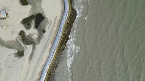 Aerial view of small sea waves crashing onto a geo-bag barrier along the shoreli Stock Footage 287779174