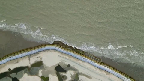 Aerial view of small sea waves crashing onto a geo-bag barrier along the shoreli Stock Footage 287779489