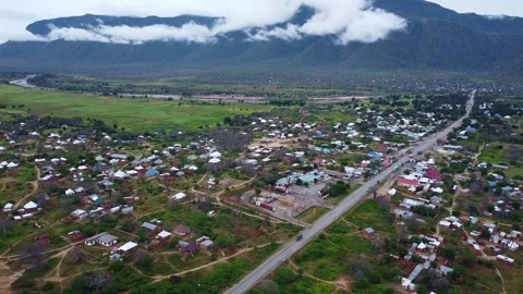 Aerial view of a small town with a mountain range covered in clouds in the Stock Footage 313316976