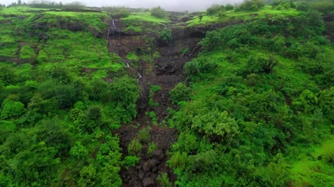 Aerial View of a Small Waterfall Cascading Through Lush Green Mountains Видео 342701567