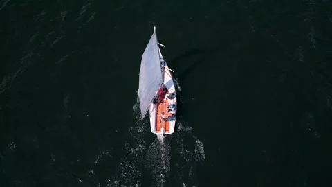 Aerial view of a small white sailing boat with crew onboard moving through dark Stock Footage 308172911
