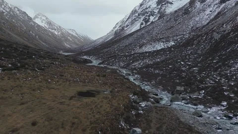 Aerial view of snow-capped mountains with flowing river, camera pans smoothly Video stock 320396254