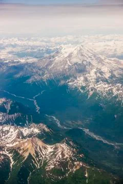 Aerial view of snow-capped peaks surrounding a green river valley, Aleutian Rang Stock Photos