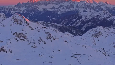 Aerial view of snow covered mountain crests alight with dawn vivid colors Stock Footage 313367657