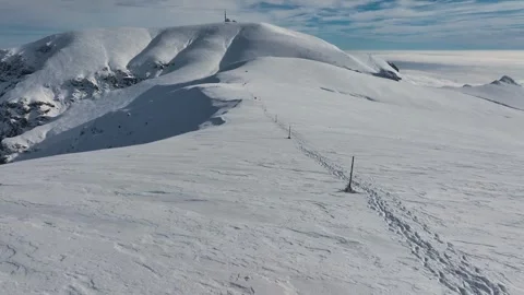 Aerial view of a snow-covered mountain summit with a marked trail Stock Footage 343569752