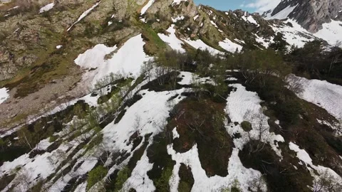 Aerial view of snow-covered mountains with trees and rocky terrain in spring Stock Footage 340524846
