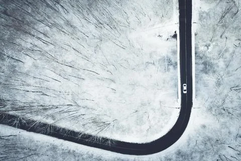 Aerial view of snowy forest while car drives on a icy road. Captured from above  Stock Photos