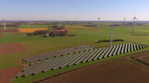 Aerial view of a solar panel farm and wind turbines in green fields. Drone Stock Footage 337562750