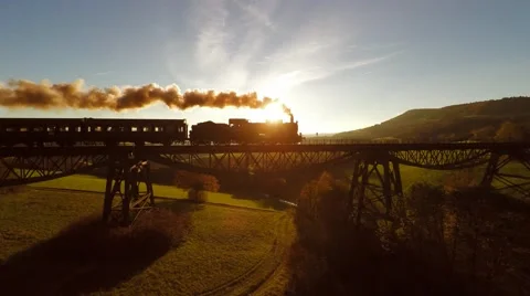 Aerial view of steam engine locomotive crossing bridge at sunset magic hour Stock Footage 64541578