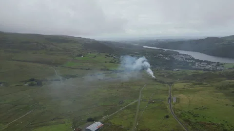 Aerial view of a steam train passing on green hills by a river. Stock Footage 314348120