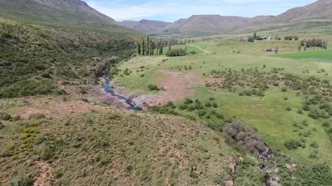 Aerial view of a stream running through lush green mountainous terrain Stock Footage 214354382