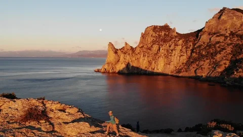 Aerial view sun sets in pink sky behind cliffs and blue sea Video stock 103835713