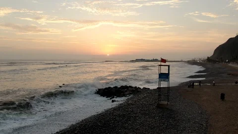 Aerial view of the sunset, on the beach, the waves break near a lifeguard tent. Video stock 128556503