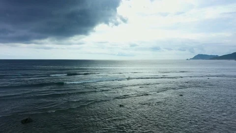 Aerial view of a sunset behind dark grey clouds. Flying slowly above dark ocean Video stock 129280323