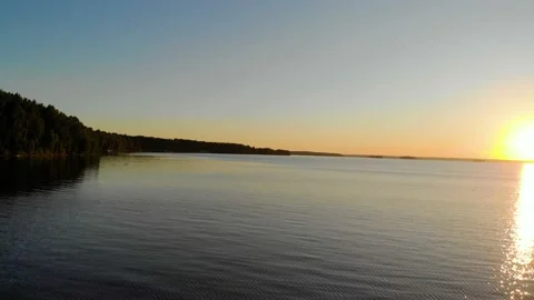 Aerial view of sunset on clear deep blue lake. Thick lush trees grow on the Видео 156225018