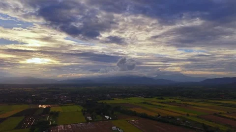 Aerial view of sunset over rice fields and mountains under a dramatic sky Stock Footage 334925689