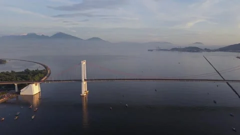 Aerial view of suspension bridge over calm coastal waters at sunrise 库存影片 340875161