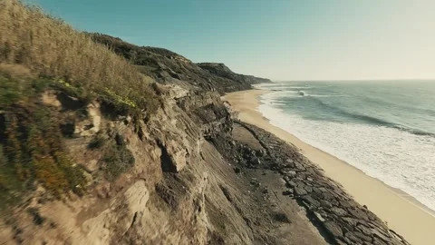 Aerial view sweeps along rugged cliffs and sandy shore Stock Footage 341825916