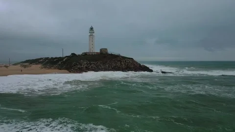 Aerial view of a tall white lighthouse perched on a rocky hill by the sea. Stock Footage 297635881