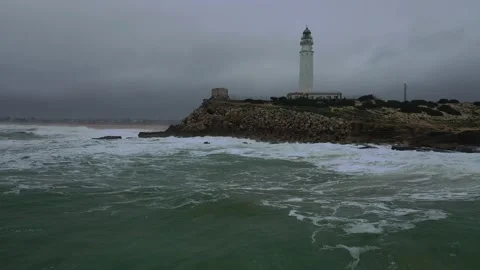 Aerial view of a tall white lighthouse perched on a rocky hill by the sea. Stock Footage 297635882