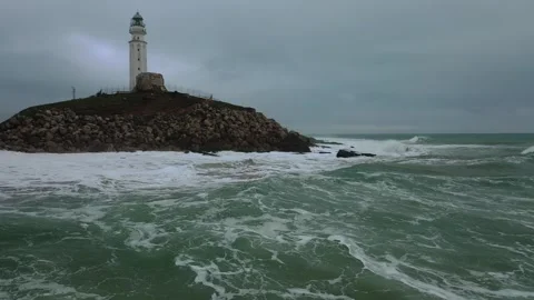 Aerial view of a tall white lighthouse perched on a rocky hill by the sea. Stock Footage 297635888