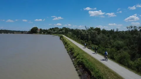 Aerial view of three cyclists riding along a river dam in summer 库存影片 338297630