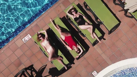 Aerial view of three girls lying under the sun near pool Stock Footage
