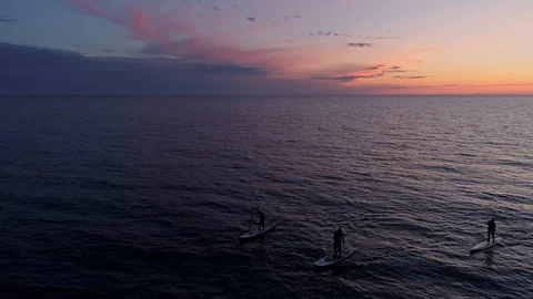 Aerial view three men rowing on SUP paddle boards in sea during amazing sunset Stock Footage 105808744