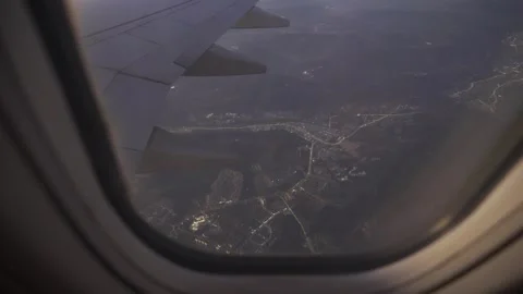 Aerial view through plane window with view of city below and plane wing in .. Видео 335582628