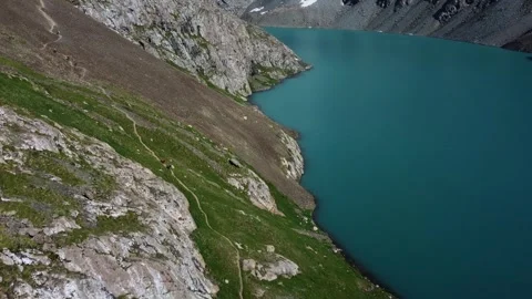 Aerial View of Tiny Hikers on Narrow Cliff Trail by Turquoise Lake Stock Footage 332204767
