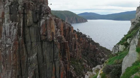 Aerial view of towering columnar rock cliffs beside a broad body of water Tasman Stockbeeldmateriaal 343704305