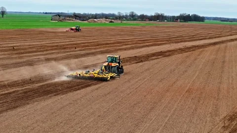 Aerial view of a tractor cultivating a large farmland field, raising dust as it Stock Footage 333999533