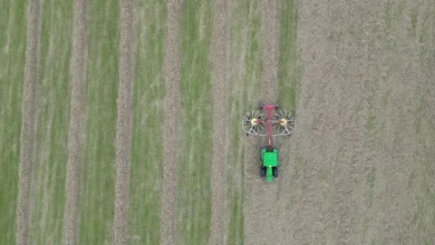 Aerial view of tractor in field pulling hay tedder moving grass into rows Stock Footage 276963398