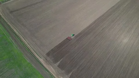 Aerial view of a tractor plowing a large field, creating distinct patterns in Stock Footage 289111972