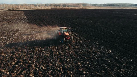 Aerial view of tractor plows the field in sunset, sunrise, raising dust, and Stock Footage 128382432