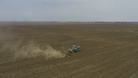 Aerial view tractor plows a large field. Dust in shot. Seagulls sits on field Stock Footage 118742945