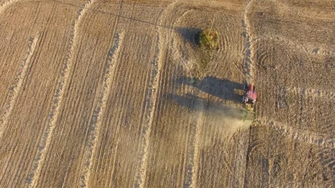 Aerial view of tractor pulling a baling machine across flat farmland at Stock Footage 97145238